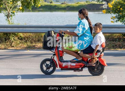 SAMUT PRAKAN, THAILANDIA, 15 dicembre 2023, Una donna guida un ragazzo in uniforme scolastica su una moto elettrica Foto Stock