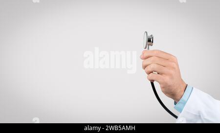 Mano maschio che regge stetoscopio su sfondo liscio, spazio libero Foto Stock