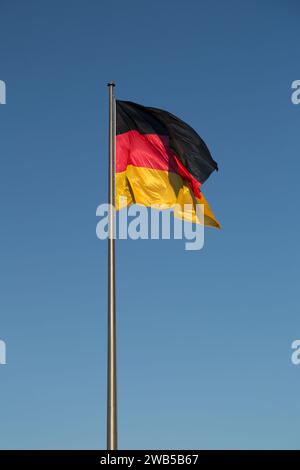 Bandiera tedesca su un'asta di bandiera contro il cielo blu, bandiera nazionale della Germania. Foto Stock