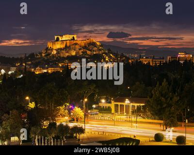 Vista sulla collina dell'Acropoli dallo stadio Panathenaic al tramonto. Foto a lunga esposizione con percorsi luminosi in strada. Atene, Grecia Foto Stock