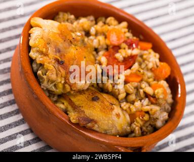 Porridge d'orzo con cosce di pollo in recipiente di ceramica Foto Stock