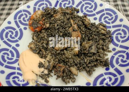 Concediti una sinfonia di sapori con questo squisito piatto caratterizzato da teneri calamari, succulenti gamberi e riso nero adornato con una dozzina di cremoso Foto Stock
