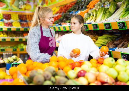 Donna negozio di alimentari impiegato aiuta adolescente ragazza raccogliere frutta Foto Stock