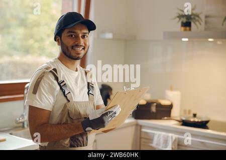 Ritratto di un giovane riparatore sorridente in piedi con appunti in cucina a casa Foto Stock