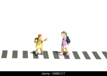 Fotografia in miniatura di giocattoli per persone piccole. Due studenti dell'asilo che camminano sopra l'attraversamento della zebra. Isolato su sfondo bianco. Foto immagine Foto Stock