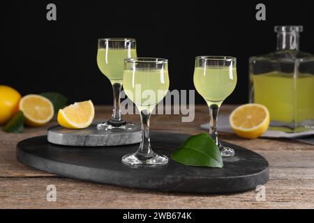 Gustoso liquore al limoncello, limoni e foglie verdi su tavola di legno Foto Stock