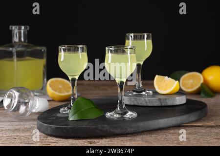 Gustoso liquore al limoncello, limoni e foglie verdi su tavola di legno Foto Stock