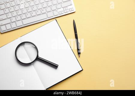 Libro aperto vuoto, lente di ingrandimento, tastiera e penna su sfondo giallo. Celebrazione della Giornata Mondiale della Poesia Foto Stock