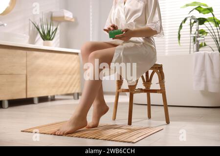 Giovane donna che tiene un vaso di gel di aloe in bagno, primo piano Foto Stock