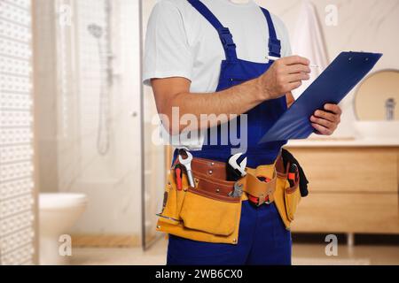 Idraulico con clipboard e cintura portautensili in bagno, primo piano. Spazio per il testo Foto Stock