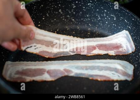 Friggere tre fette di pancetta nella padella. Foto Stock