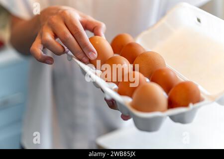 donne con in mano una scatola di uova di cartone piena di uova. la ragazza prende un uovo di gallina da una scatola bianca Foto Stock