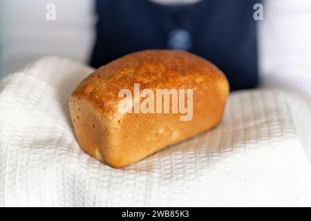 Una donna anziana tratta il pane. le mani della nonna tengono il pane sul lato dell'asciugamano bianco sembrano casalinghi dolci da forno caldi e gustosi Foto Stock