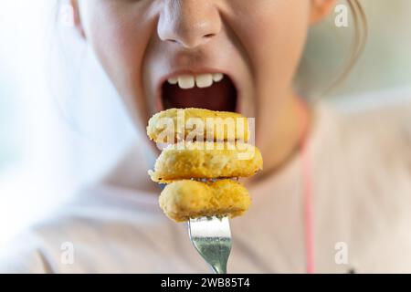 Deliziose pepite di pollo. Una ragazza adolescente sta mangiando pepite su una forchetta. Foto Stock