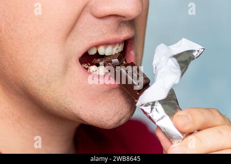 Bocca dell'uomo che mangia cioccolato su sfondo blu. Foto Stock