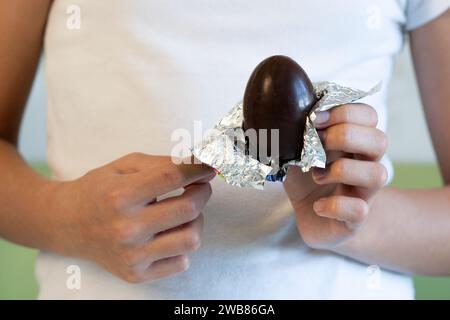 Un bambino apre un uovo di cioccolato, un uovo di cioccolato nelle mani di una ragazza adolescente da vicino Foto Stock