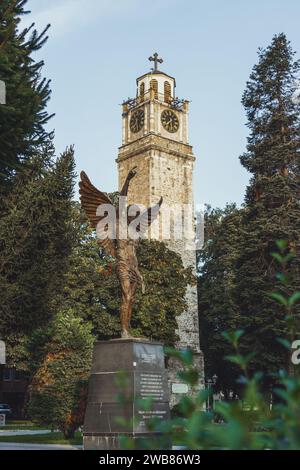 La torre dell'orologio di epoca ottomana nella città di Bitola, in Macedonia del Nord, con una statua di un angelo di fronte ad essa. Preso in una mattinata di sole con cielo blu Foto Stock