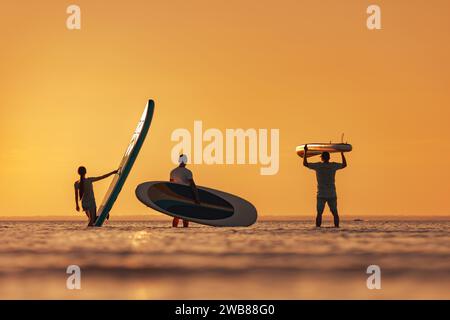 Le sagome di tre amici si trovano in un lago calmo con le tavole sup in mano Foto Stock