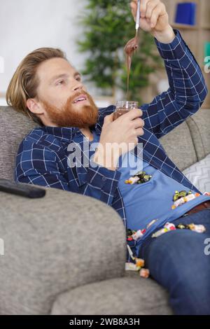 uomo coperto di dolci che mangiano cioccolato sparso dal vaso Foto Stock