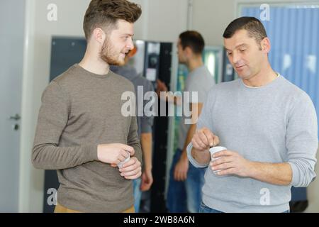 due uomini che chiacchierano tenendo tazze usa e getta dal distributore automatico Foto Stock