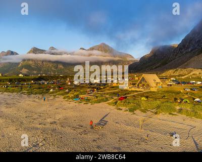 Vista aerea sulla spiaggia di Lofoten, sotto il sole di mezzanotte, sulla spiaggia di Skagsanden. Sole e nuvole di montagna basse. Campeggio, ristorante. Foto Stock