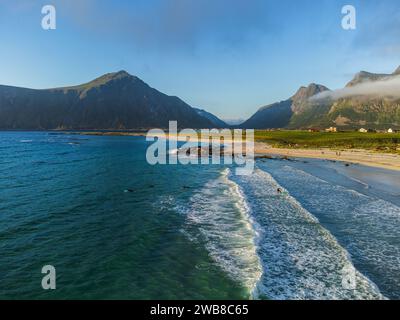 Vista aerea sulla spiaggia di Skagsanden vicino al Lofoten Beach Camp sotto il sole di mezzanotte, il sole e le nuvole basse di montagna. Turisti sulla spiaggia. Foto Stock