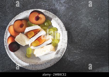Formaggio Camembert brie con uva e prugne. Camembert e brie, tagliati a pezzetti. Formaggio servito su piatti fatti a mano. Vista dall'alto, distributore piatto Foto Stock
