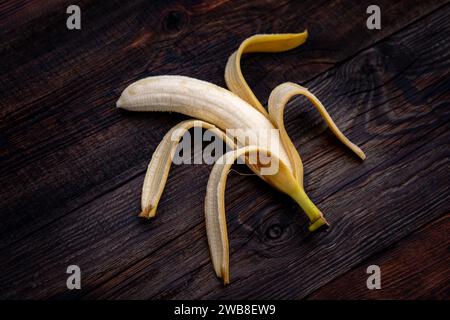 Banana strammatura appena sbucciata con macchie, su un tavolo di legno Foto Stock