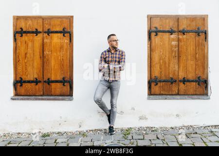 Giovane camicia da uomo d'affari si appoggia alla schiena contro il muro di una casa bianca nel centro storico di Sighisoara Foto Stock