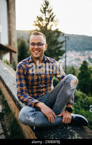 Un giovane in camicia siede sorridente su un muro del castello Foto Stock