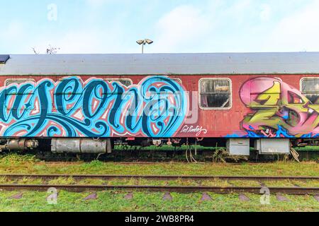 AS, Limburgo, Belgio. 17 dicembre 2023. Molto vecchia autovettura in lamiera rossa con porte e finestre dipinte con lettere blu, numeri in giallo e rosa Foto Stock