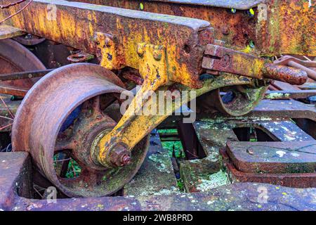 Primo piano di una ruota sul vecchio carrello, supporto e assale centrale, impilata su un'enorme struttura in acciaio arrugginito, danneggiata, corrosa dal passare del tempo, indust Foto Stock