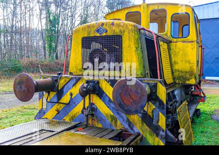 Parte posteriore della vecchia cabina di controllo del treno in rovina gialla sui binari in disuso presso la vecchia stazione, fermi di accoppiamento e piattaforma di carico piana, meta arrugginita e corrosa Foto Stock