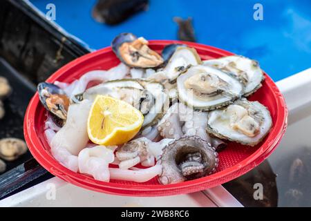 Piatto di plastica con pezzi crudi di polpo, seppie, cozze nere, ostriche, limone, pronto a mangiare, in un mercato di Street food a Bari, Puglia, Italia Foto Stock