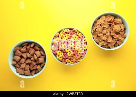 Varietà di cereali in ciotole blu, colazione veloce su sfondo giallo. Vista dall'alto Foto Stock