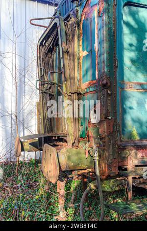 Vista laterale dei tamponi di collegamento e della porta caduta di una carrozza ferroviaria fatiscente, arrugginita, danneggiata e abbandonata, vernice sbucciata, binari in disuso Foto Stock