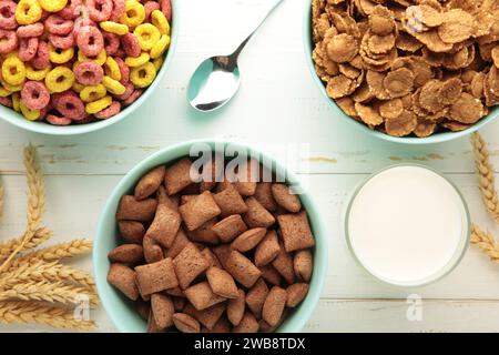 Varietà di cereali in ciotole blu, colazione veloce e latte su fondo di legno bianco. Vista dall'alto Foto Stock