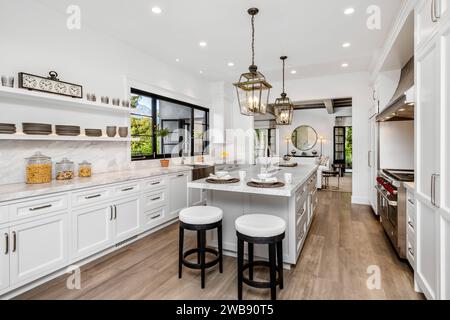 Un moderno interno della cucina presenta armadi bianchi ed elettrodomestici in acciaio inox disposti su un pavimento in legno Foto Stock