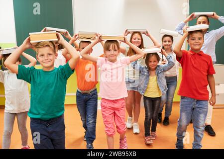 Ritratto di diversi studenti scolastici che bilanciano libri a testa con insegnante donna durante l'attività in classe Foto Stock