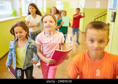 Ritratto di una ragazza sorridente che tiene un libro mentre correva in corridoio con gli amici durante la pausa a scuola Foto Stock
