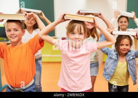 Ritratto di bambini sorridenti che bilanciano i libri sulla testa in classe Foto Stock