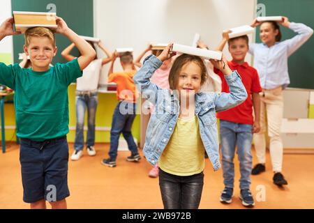 Ritratto di una studentessa sorridente che bilancia il libro con i compagni di classe mentre si trova in classe Foto Stock