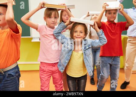 Ritratto di scolari sorridenti che bilanciano i libri sulla testa durante l'attività in classe Foto Stock