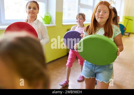 Ritratto delle studentesse che tengono cuscini colorati mentre camminano nel corridoio della scuola Foto Stock