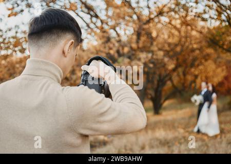 Fotografo professionista di matrimoni che scatta foto della sposa e dello sposo nella natura in autunno Foto Stock