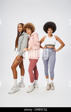 Graziose amiche afro-americane in abbigliamento sportivo che guardano la fotocamera su sfondo grigio, Giuneteenth Foto Stock