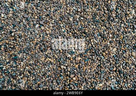 Piccola trama di pietra per lo sfondo. Sfondo ghiaioso. Liscia la trama dei ciottoli rotondi. Vista ravvicinata della spiaggia di Pebble Sea, ciottoli umidi scuri e dr. Grigio Foto Stock