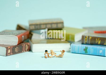 Fotografia di figure giocattolo in miniatura. Leggi il concetto. Gruppo di neonati seduti davanti alla pila del libro. Isolato su sfondo blu. Foto Stock