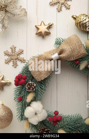 Corona di abeti, pini e ramoscelli di abete rosso, decorata con cotone, fiori e decorazioni natalizie su sfondo di legno bianco. Foto verticale. Vista dall'alto Foto Stock