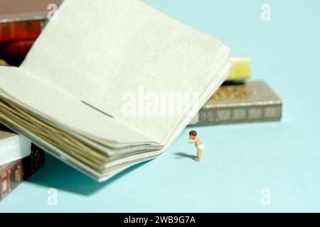 Fotografia di figure giocattolo in miniatura. Leggi il concetto. Un bambino in piedi di fronte a un libro di storie aperto. Isolato su sfondo blu. Imag Foto Stock